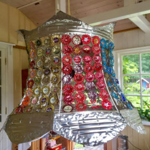 Lampskärm dekorerad med kapsyler i olika färger.